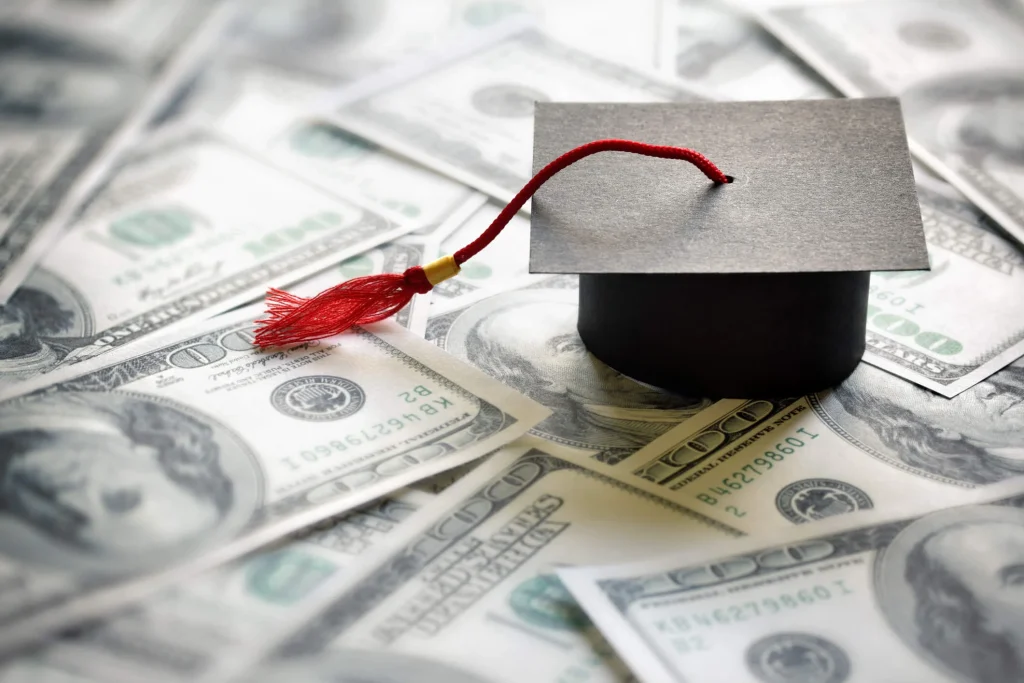 This is a photo of a graduation cap on top of a bunch of hundred dollar bills representing college debt that could be paid with title loans