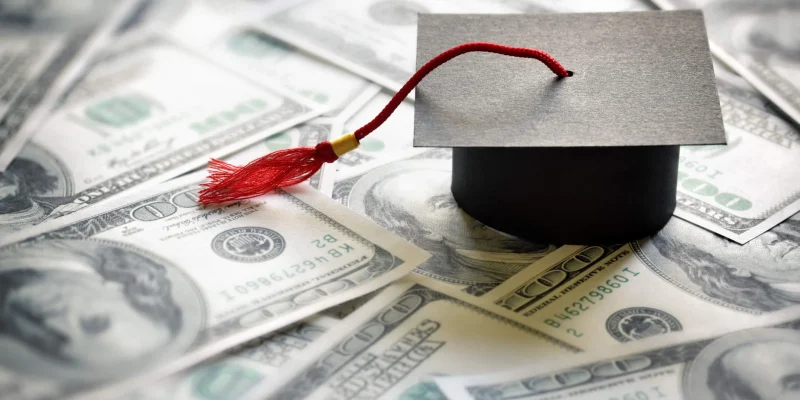 This is a photo of a graduation cap on top of a bunch of hundred dollar bills representing college debt that could be paid with title loans