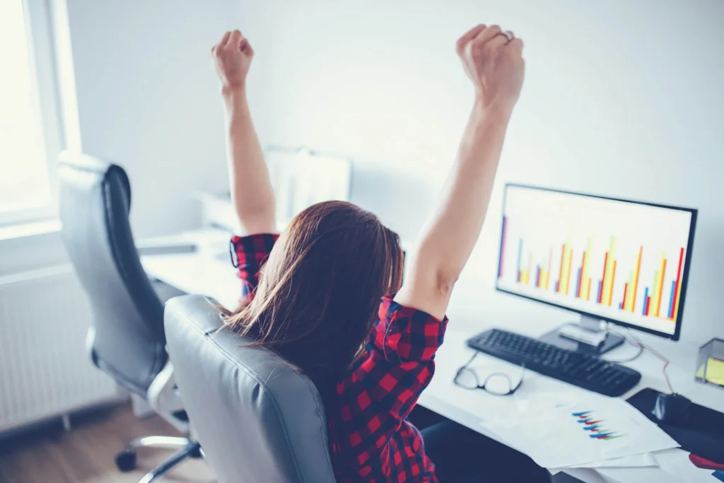 This is a photo of a woman cheering behind a computer wearing a plaid shirt, celebrating thee benefits of a title loan