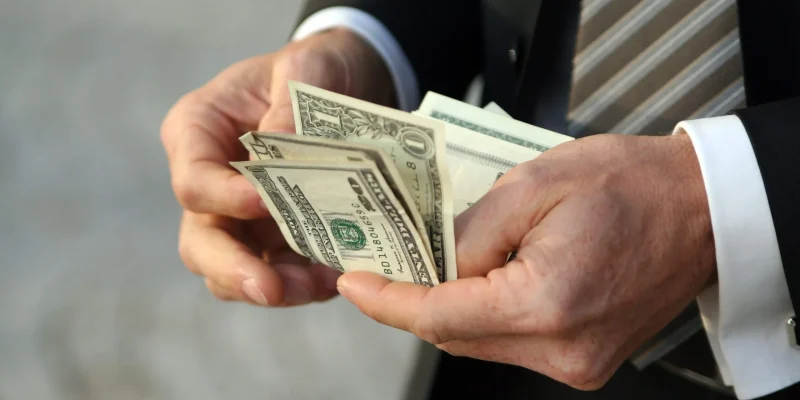 This is a photo of a man in a suit counting his cash, which represents people avoiding overpaying for title loans