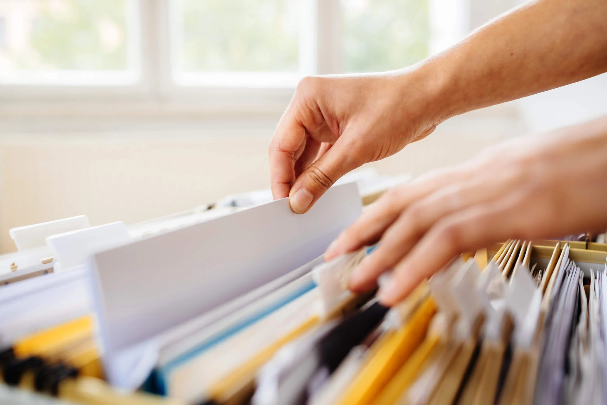 this is a photo of a person's hands sifting through paperwork in a file cabinet