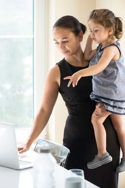 photo of a woman holding her daughter and looking at her laptop