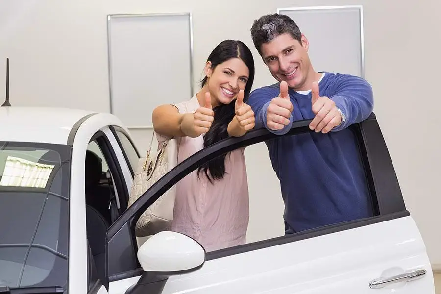 photo of two people buying a car smiling and giving a thumbs up